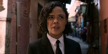 Movie still from “Men in Black: International” (2019), directed by F. Gary Gray – A woman wearing a suit and tie standing in front of a building; Close Up shot, Over the shoulder angle