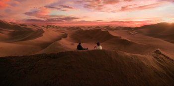 Movie still from “Men in Black: International” (2019), directed by F. Gary Gray – Two people sitting on top of a sand dune at sunset; Extreme Wide shot, High angle