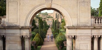 Movie still from “Men in Black: International” (2019), directed by F. Gary Gray – Two people walking through an archway in a garden; Extreme Wide shot, High angle