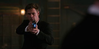 Movie still from “Men in Black: International” (2019), directed by F. Gary Gray – A man in a black suit holding a blue object; Medium shot, Over the shoulder angle
