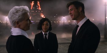 Movie still from “Men in Black: International” (2019), directed by F. Gary Gray – Two men and a woman standing in front of the eiffel tower at night; Medium shot, Over the shoulder angle