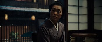 Movie still from “Midway” (2019), directed by Roland Emmerich – A person wearing a robe sitting in front of a building; Medium shot, Over the shoulder angle