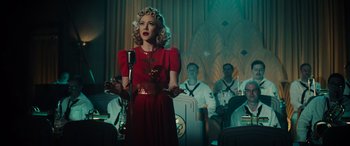 Movie still from “Midway” (2019), directed by Roland Emmerich – A woman in a red dress singing into a microphone in front of other people; Medium shot, Over the shoulder angle