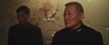 Movie still from “Midway” (2019), directed by Roland Emmerich – An older man wearing a black shirt looking at the camera; Close Up shot, Over the shoulder angle