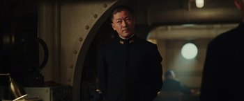 Movie still from “Midway” (2019), directed by Roland Emmerich – A man in a black suit standing next to an archway; Medium shot, Low angle