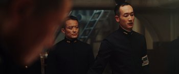 Movie still from “Midway” (2019), directed by Roland Emmerich – A man in a black suit standing next to another man in a black suit; Medium shot, Low angle