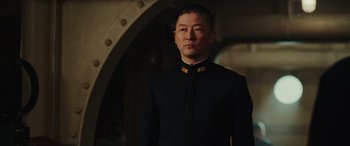 Movie still from “Midway” (2019), directed by Roland Emmerich – A man in a black suit standing in front of an archway; Medium shot, Low angle