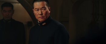 Movie still from “Midway” (2019), directed by Roland Emmerich – An older man wearing a black jacket and a gold neck tie; Close Up shot, Low angle