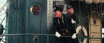 Movie still from “Midway” (2019), directed by Roland Emmerich – Two men dressed in black uniforms and white gloves look out of a train window; Medium shot, Low angle