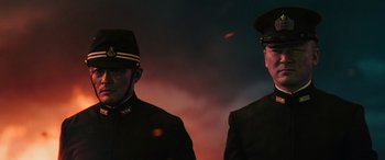Movie still from “Midway” (2019), directed by Roland Emmerich – Two men standing next to each other in front of a dark background; Medium shot, Low angle