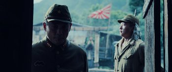 Movie still from “Midway” (2019), directed by Roland Emmerich – Two men in military uniforms stand in front of a japanese flag; Medium shot, Over the shoulder angle