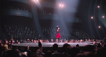 Movie still from “Minions” (2015), directed by Pierre Coffin – A woman in a red dress on a stage in front of an audience; Extreme Wide shot, Over the shoulder angle