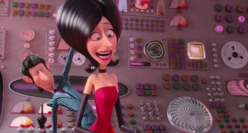Movie still from “Minions” (2015), directed by Pierre Coffin – A woman in a red dress is standing in front of a computer keyboard; Medium shot, High angle