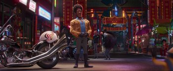 Movie still from “Minions: The Rise of Gru” (2022), directed by Jonathan del Val – A man standing next to a motorcycle on a city street; Wide shot, Low angle