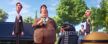Movie still from “Minions: The Rise of Gru” (2022), directed by Jonathan del Val – A man in a suit and tie standing next to a woman; Medium shot, Over the shoulder angle