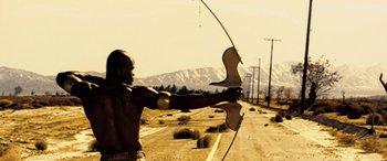 Movie still from “Minority Report” (2002), directed by Steven Spielberg – A man holding a bow and arrow in the middle of a road; Medium shot, Low angle