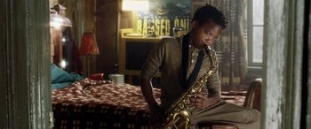 Movie still from “Minority Report” (2002), directed by Steven Spielberg – A man sitting on the ground playing a saxophone; Medium shot, Low angle