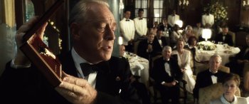 Movie still from “Minority Report” (2002), directed by Steven Spielberg – An older man in a suit and bow tie in front of a group of people; Close Up shot, Over the shoulder angle