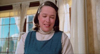 Movie still from “Misery” (1990), directed by Rob Reiner – A woman with a cross on her head smiling; Close Up shot, Low angle