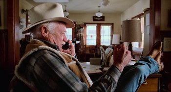 Movie still from “Misery” (1990), directed by Rob Reiner – An older man sitting at a table talking on a cell phone; Medium shot, Low angle