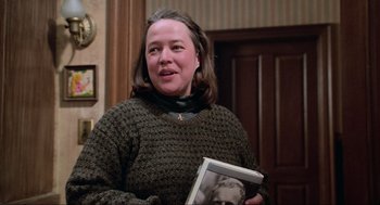 Movie still from “Misery” (1990), directed by Rob Reiner – A woman in a sweater holding a book; Medium shot, Over the shoulder angle