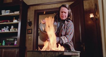 Movie still from “Misery” (1990), directed by Rob Reiner – A woman in a plaid shirt is cooking on a fire; Medium shot, Low angle