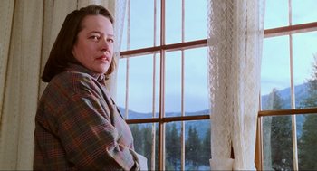 Movie still from “Misery” (1990), directed by Rob Reiner – A woman standing in front of a window looking out at the mountains; Close Up shot, Low angle