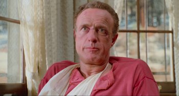 Movie still from “Misery” (1990), directed by Rob Reiner – An older man wearing a pink shirt and a towel around his neck; Close Up shot, Low angle