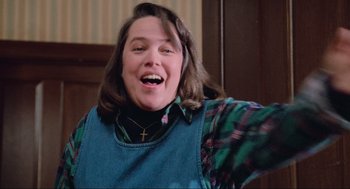 Movie still from “Misery” (1990), directed by Rob Reiner – A woman with a cross on her shirt is making a funny face; Medium shot, Low angle