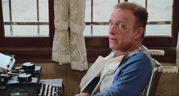 Movie still from “Misery” (1990), directed by Rob Reiner – A man sitting in front of a typewriter in front of a window; Close Up shot, Low angle