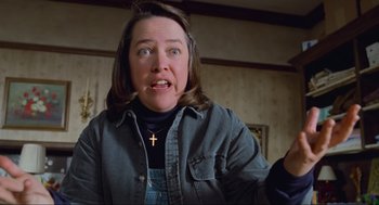 Movie still from “Misery” (1990), directed by Rob Reiner – A woman with a cross on her neck is looking at the camera; Medium shot, Low angle