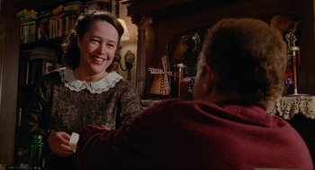 Movie still from “Misery” (1990), directed by Rob Reiner – A woman smiles at a man sitting in front of a fireplace; Medium shot, Over the shoulder angle
