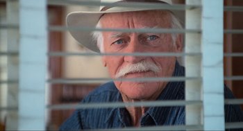 Movie still from “Misery” (1990), directed by Rob Reiner – An older man with a hat looking through a window; Close Up shot, Low angle
