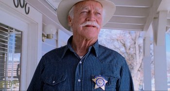 Movie still from “Misery” (1990), directed by Rob Reiner – An older man wearing a cowboy hat with a sheriff's badge on it; Close Up shot, Low angle