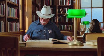 Movie still from “Misery” (1990), directed by Rob Reiner – An older man sitting at a desk reading a book; Medium shot, Low angle