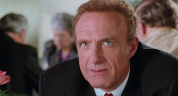 Movie still from “Misery” (1990), directed by Rob Reiner – A man in a suit and red tie looking at the camera; Close Up shot, Low angle