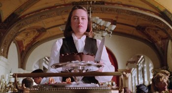 Movie still from “Misery” (1990), directed by Rob Reiner – A woman holding a large knife in front of a cake on top of a cake plate; Medium shot, Low angle