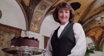 Movie still from “Misery” (1990), directed by Rob Reiner – A woman standing in front of a cake on a platter; Medium shot, Low angle