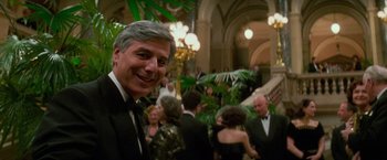 Movie still from “Mission: Impossible” (1996), directed by Brian De Palma – A man in a tuxedo smiling at the camera; Medium shot, Over the shoulder angle