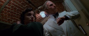 Movie still from “Mission: Impossible” (1996), directed by Brian De Palma – An older man in a white suit and a woman in a green dress; Medium shot, Low angle