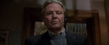 Movie still from “Mission: Impossible” (1996), directed by Brian De Palma – An older man wearing a suit and tie with a headset on; Close Up shot, Low angle
