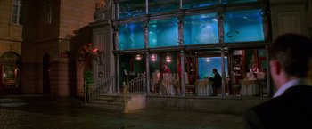 Movie still from “Mission: Impossible” (1996), directed by Brian De Palma – People are sitting at tables outside of an aquarium; Extreme Wide shot, High angle