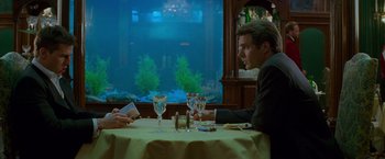 Movie still from “Mission: Impossible” (1996), directed by Brian De Palma – Two people sitting at a dinner table in front of an aquarium; Medium shot, Over the shoulder angle