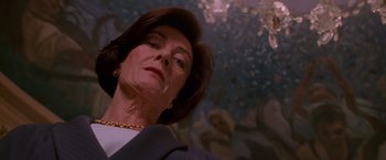 Movie still from “Mission: Impossible” (1996), directed by Brian De Palma – An older woman in a blue jacket and a gold necklace; Close Up shot, Low angle