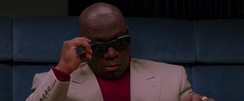 Movie still from “Mission: Impossible” (1996), directed by Brian De Palma – A man in a red shirt and a tan jacket wearing a pair of sunglasses; Close Up shot, Low angle