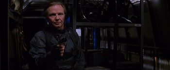 Movie still from “Mission: Impossible” (1996), directed by Brian De Palma – A man holding a gun while standing in a room; Medium shot, Over the shoulder angle