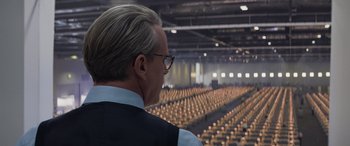 Movie still from “Mission: Impossible - Dead Reckoning Part One” (2023), directed by Christopher McQuarrie – An older man in a large auditorium looking out the window; Medium shot, Over the shoulder angle