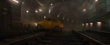 A yellow car is driving down the train tracks in a tunnel