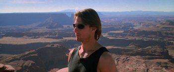 Movie still from “Mission: Impossible II” (2000), directed by John Woo – A man with sunglasses is standing on top of a mountain; Close Up shot, Low angle