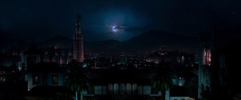 A full moon rises over a city at night with palm trees in the foreground